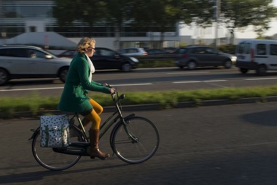vrouw op de fiets langs drukke weg