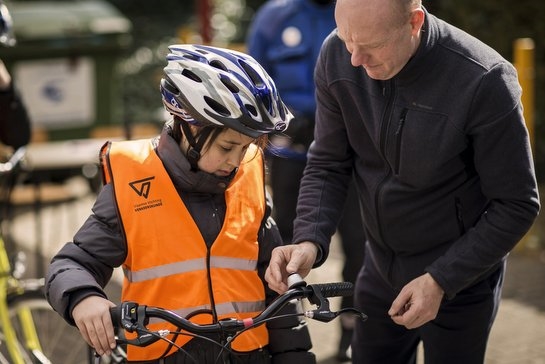 kind op de fiets met fietshelm en veiligheidshesje wordt geholpen door mobicoach 
